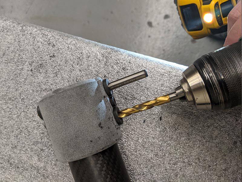 Carbon fiber tube with metallic end-cap bonded assembly on a work surface. Technician is drilling into an alignment fixture on the end-cap.